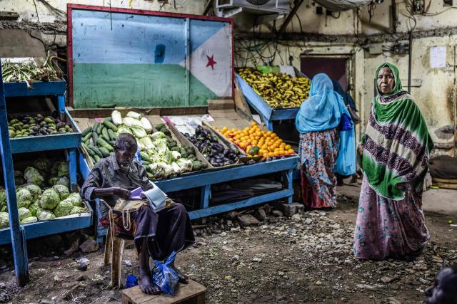 A vegetable seller waits for customers at his stall decorated with the Djiboutian flag in an open-air market as residents take to the streets during the cooler evening hours to escape the daytime heat in downtown Djibouti, on April 7, 2026, ahead of the 2026 Djiboutian presidential elections. (Photo by Luis TATO / AFP)