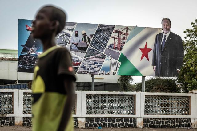 A resident stands in front of an electoral banner in support of Djibouti’s incumbent president and presidential candidate Ismail Omar Guelleh in Djibouti, on April 8, 2026, ahead of the 2026 Djiboutian presidential elections. (Photo by Luis TATO / AFP)