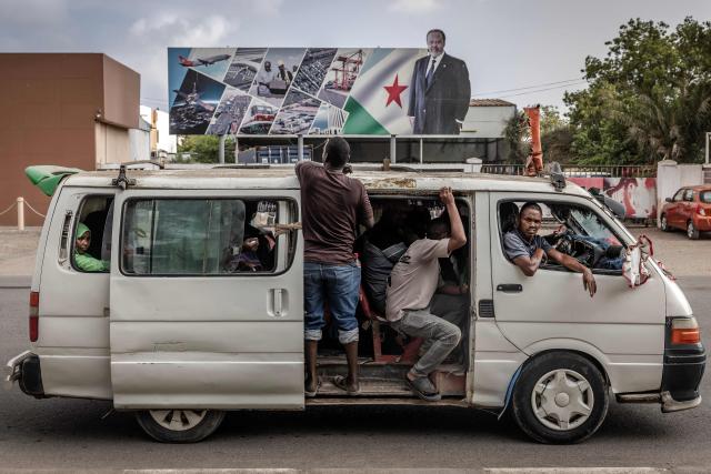 Residents board a minibus in front of an electoral banner in support of Djibouti’s incumbent president and presidential candidate Ismail Omar Guelleh in Djibouti, on April 8, 2026, ahead of the 2026 Djiboutian presidential elections. (Photo by Luis TATO / AFP)