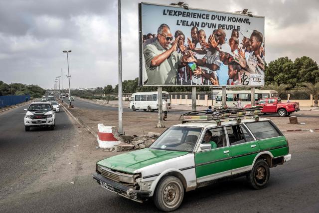 A taxi driver drives his taxi past an electoral banner in support of Djibouti’s incumbent president and presidential candidate Ismail Omar Guelleh in Djibouti, on April 8, 2026, ahead of the 2026 Djiboutian presidential elections. (Photo by Luis TATO / AFP)