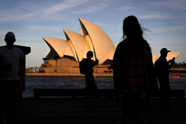 Tourists walk in front of the Sydney Opera House on an Autumn day in Sydney on April 8, 2026. (Photo by DAVID GRAY / AFP)