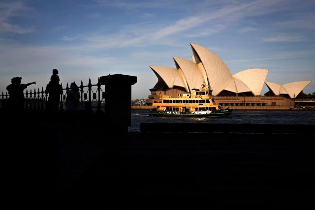 Tourists react as a ferry passes in front of the Sydney Opera House on an Autumn day in Sydney on April 8, 2026. (Photo by DAVID GRAY / AFP)