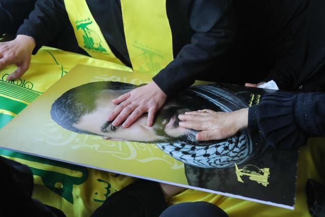 Mourners lay their hands on the portrait of a Hezbollah fighter during his funeral at a temporary graveyard in Choueifat, south of Beirut, on April 8, 2026. Israel's military said on April 8, its forces would continue their campaign against Hezbollah fighters, claiming the ceasefire with Iran does not apply to Lebanon. (Photo by ibrahim AMRO / AFP)