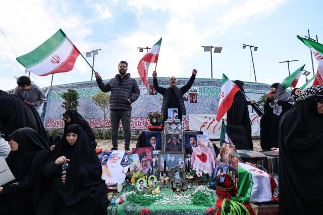 Iranians wave national flags next to a makeshift memorial as they gather in Tehran's Revolution Square after the United States and Iran agreed to a two-week ceasefire, on April 8, 2026. The United States and Iran agreed to a two-week ceasefire barely an hour before the US president's April 8 deadline to obliterate the country, triggering global relief alongside apprehension. (Photo by ATTA KENARE / AFP) / 