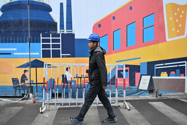 A worker walks past a board at a construction site for a futuristic innovation hub project in Shougang area, Shijingshan district in Beijing on April 8, 2026. (Photo by ADEK BERRY / AFP)
