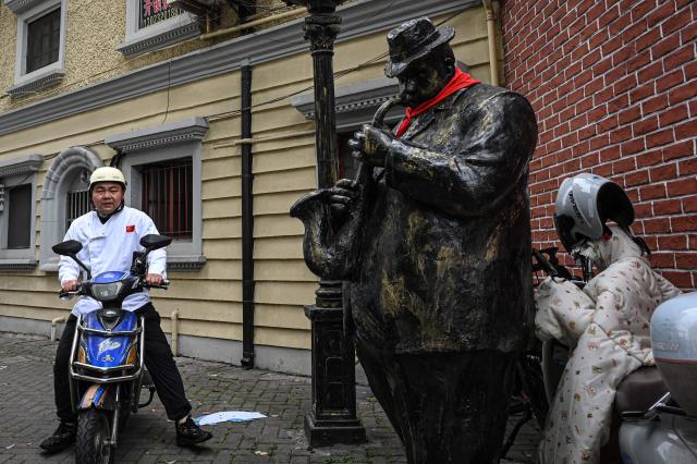 A man rides a scooter past a statue along a street in Shanghai on April 8, 2026. (Photo by Jade GAO / AFP)
