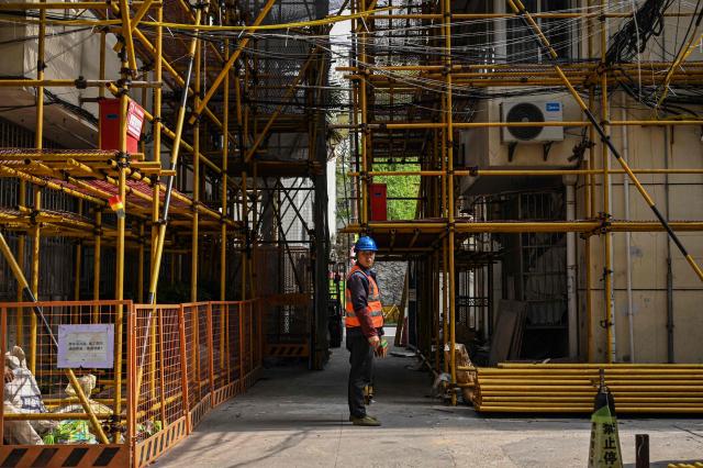 A worker stands in front of a residential building under renovation in Shanghai on April 8, 2026. (Photo by Jade GAO / AFP)