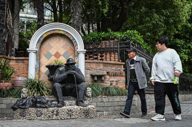 People walk past a statue along a street in Shanghai on April 8, 2026. (Photo by Jade GAO / AFP)