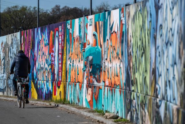 A man cycles along the recently unveiled "Sued Ost Galerie" open air collaborative graffiti art exhibition in Berlin on April 8, 2026. The 450-metre-long noise protection wall located in the capital's south east features mural art by some 20 artists collaborating around German rapper and street artist Akte One (Mark Marquardt) who initiated the project in 2025. (Photo by John MACDOUGALL / AFP)