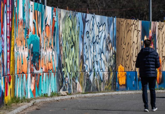 A man walks along the recently unveiled "Sued Ost Galerie" open air collaborative graffiti art exhibition in Berlin on April 8, 2026. The 450-metre-long noise protection wall located in the capital's south east features mural art by some 20 artists collaborating around German rapper and street artist Akte One (Mark Marquardt) who initiated the project in 2025. (Photo by John MACDOUGALL / AFP)