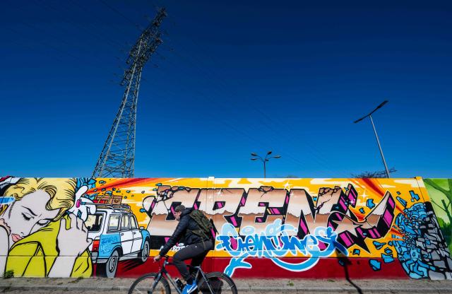 A man cycles along the recently unveiled "Sued Ost Galerie" open air collaborative graffiti art exhibition in Berlin on April 8, 2026. The 450-metre-long noise protection wall located in the capital's south east features mural art by some 20 artists collaborating around German rapper and street artist Akte One (Mark Marquardt) who initiated the project in 2025. (Photo by John MACDOUGALL / AFP)
