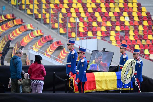 A family pays their respects as honor guard soldiers stand next to the coffin of Romanian football legend Mircea Lucescu as it is laid in state at the National Arena in Bucharest, Romania, April 8, 2026. Fans and figures from the sporting world gathered at the country's largest stadium to pay their final respects to the former national team coach and one of the most decorated managers in history, who passed away on April 7, 2026, at the age of 80. (Photo by Daniel MIHAILESCU / AFP)