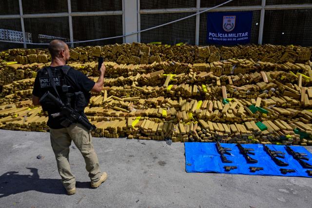 A police officer takes a photo of 48 tons of seized marijuana presented at the City of Police in Rio de Janeiro, Brazil on April 8, 2026, after they were uncovered by chance by a sniffer dog during a regular operation against criminal factions. During the operation in the Complexo da Mare, a large complex of favelas in the north of the city, a dog named Hulk indicated there was something suspicious under an abandoned water tank. An officer "discovered a bunker inside where this entire quantity of drugs had been hidden," said Lieutenant Colonel Luciano Pedro, commander of the Canine Operations Battalion. (Photo by Pablo PORCIUNCULA / AFP)