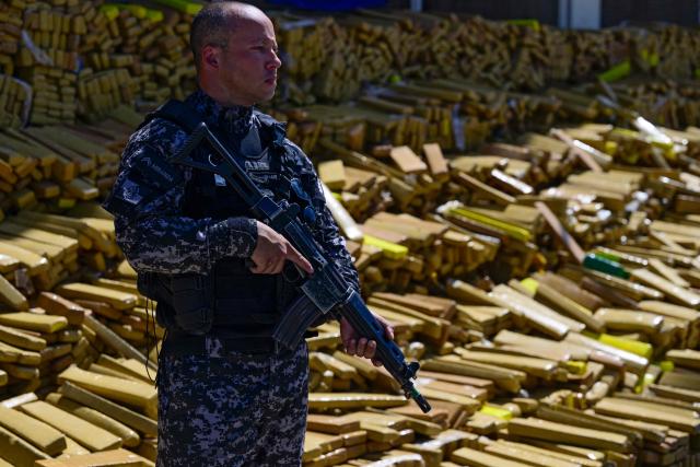 A police officer stands next to 48 tons of seized marijuana presented at the City of Police in Rio de Janeiro, Brazil on April 8, 2026, after they were uncovered by chance by a sniffer dog during a regular operation against criminal factions. During the operation in the Complexo da Mare, a large complex of favelas in the north of the city, a dog named Hulk indicated there was something suspicious under an abandoned water tank. An officer "discovered a bunker inside where this entire quantity of drugs had been hidden," said Lieutenant Colonel Luciano Pedro, commander of the Canine Operations Battalion. (Photo by Pablo PORCIUNCULA / AFP)