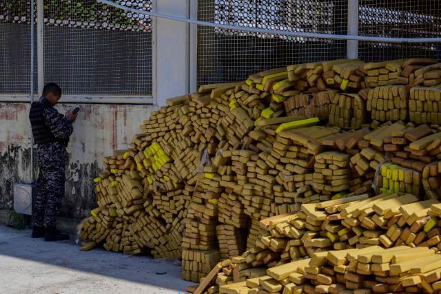 A police officer uses mobile phone next to 48 tons of seized marijuana presented at the City of Police in Rio de Janeiro, Brazil on April 8, 2026, after they were uncovered by chance by a sniffer dog during a regular operation against criminal factions. During the operation in the Complexo da Mare, a large complex of favelas in the north of the city, a dog named Hulk indicated there was something suspicious under an abandoned water tank. An officer "discovered a bunker inside where this entire quantity of drugs had been hidden," said Lieutenant Colonel Luciano Pedro, commander of the Canine Operations Battalion. (Photo by Pablo PORCIUNCULA / AFP)