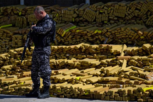 A police officer stands next to 48 tons of seized marijuana presented at the City of Police in Rio de Janeiro, Brazil on April 8, 2026, after they were uncovered by chance by a sniffer dog during a regular operation against criminal factions. During the operation in the Complexo da Mare, a large complex of favelas in the north of the city, a dog named Hulk indicated there was something suspicious under an abandoned water tank. An officer "discovered a bunker inside where this entire quantity of drugs had been hidden," said Lieutenant Colonel Luciano Pedro, commander of the Canine Operations Battalion. (Photo by Pablo PORCIUNCULA / AFP)