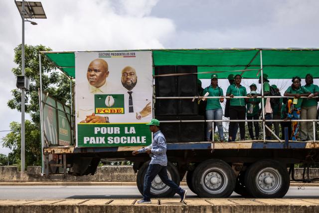 A supporter walks past a election caravane bearing a billboard of Paul Hounkpè, presidential candidate, and Judicaël Hounwanou, vice presidential candidate, of the Force Cauris pour un Benin Emergent (FCBE) party on the road to Ouidah, on April 8, 2026. (Photo by OLYMPIA DE MAISMONT / AFP)