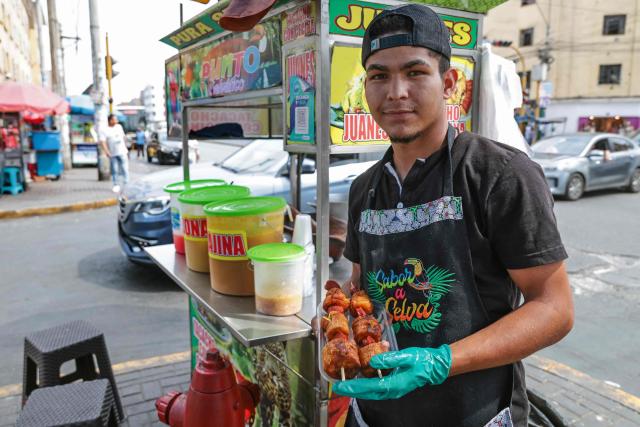 A street vendor holds skewers of fried plantain with jungle hot dog, at an Amazonian food stall in the district of La Victoria, in Lima, on April 7, 2026. (Photo by Connie FRANCE / AFP)