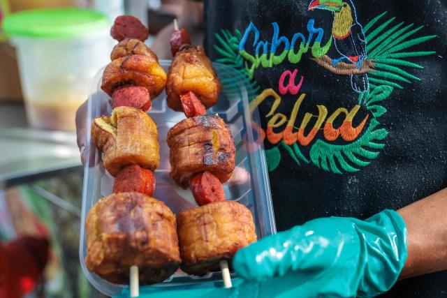 A street vendor holds skewers of fried plantain with jungle hot dog, at an Amazonian food stall in the district of La Victoria, in Lima, on April 7, 2026. (Photo by Connie FRANCE / AFP)