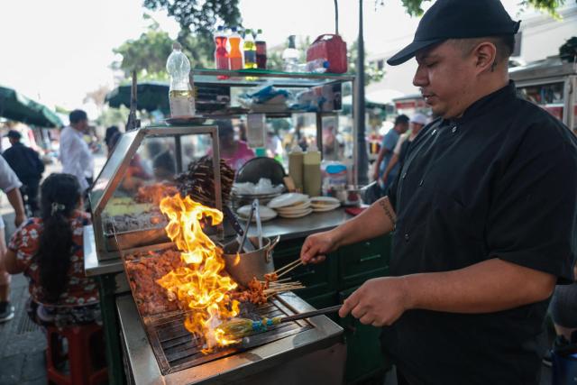 A street vendor prepares anticuchos -marinated beef heart skewers, typically grilled- with potatoes and corn, at a street food stand outside the Central Market, in Lima, on April 7, 2026. (Photo by Connie FRANCE / AFP)