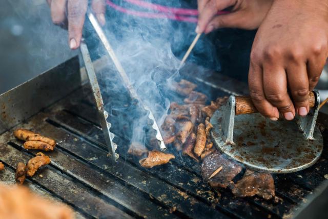 A street vendor prepares anticuchos -marinated beef heart skewers, typically grilled- with potatoes and corn, at a street food stand outside the Central Market, in Lima, on April 7, 2026. (Photo by Connie FRANCE / AFP)