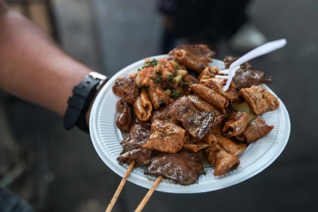 A street vendor holds a dish with anticuchos -marinated beef heart skewers, typically grilled-, rachi -marinated and grilled beef tripe (cow belly), and potatoes, at a street food stand outside the Central Market, in Lima, on April 7, 2026. (Photo by Connie FRANCE / AFP)