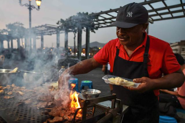 A street vendor prepares anticuchos -marinated beef heart skewers, typically grilled-  with potatoes and corn, at the Alameda Chabuca Granda in Lima, on April 7, 2026. (Photo by Connie FRANCE / AFP)