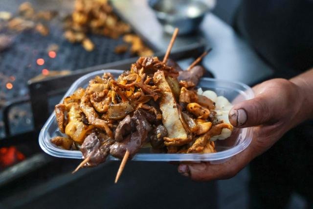 A street vendor serves a portion of anticuchos -marinated beef heart skewers, typically grilled- with potatoes and corn, at the Alameda Chabuca Granda in Lima, on April 7, 2026. (Photo by Connie FRANCE / AFP)