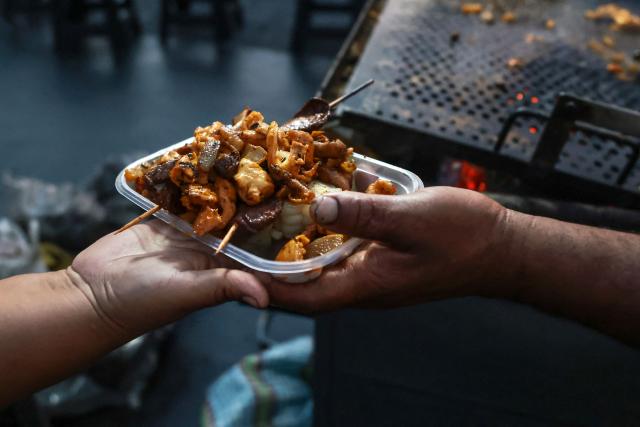 A street vendor serves a portion of anticuchos -marinated beef heart skewers, typically grilled- with potatoes and corn, at the Alameda Chabuca Granda in Lima, on April 7, 2026. (Photo by Connie FRANCE / AFP)