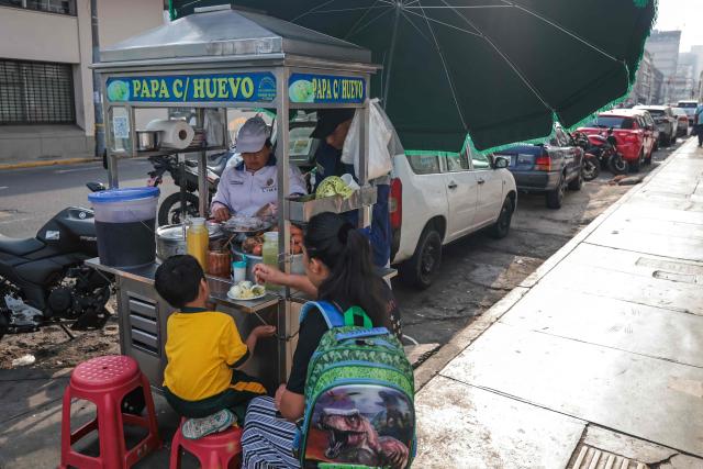 A woman and her son have potatoes with eggs for breakfast at a stall located on Jiron Quilca, in Lima on April 8, 2026. (Photo by Connie FRANCE / AFP)