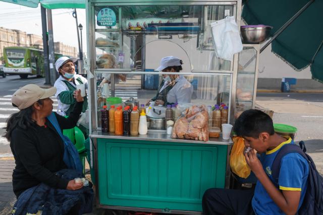 A woman and her son have bread and quinoa soda for breakfast at a stall located on Jiron Quilca, in Lima on April 8, 2026. (Photo by Connie FRANCE / AFP)