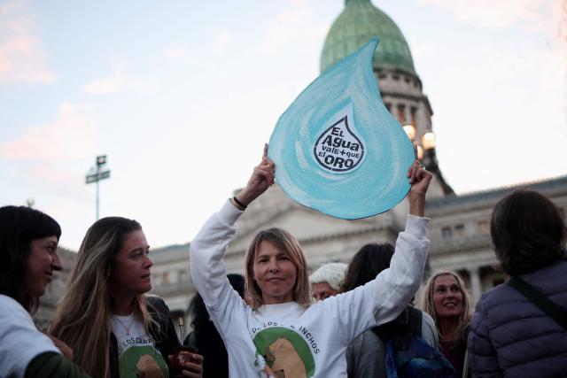 A demonstrator shows a sign depicting a water drop that reads in Spanish, "Water is worth more than gold," during a protest against the modifications in glacier law in front of the Congress building in Buenos Aires on April 8, 2026. Argentine deputies will debate on April 8, 2026 a government proposal calling on the provinces to redefine glacier protection zones in order to expand mining operations. (Photo by TOMAS CUESTA / AFP)
