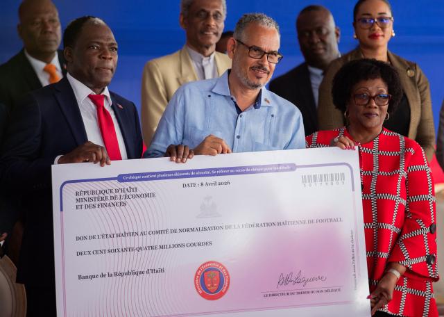 Prime Minister Alix Didier Fils-Aimй (C), Haitian Football Federation (FHF) President Marie Monique Andrй (R), and Sports Minister Pythagore Dumas (L) hold a check during a presentation to the Haitian Football Federation for World Cup qualification bonuses and team preparations at the Villa d’accueil in Port-au-Prince, on April 8, 2026. (Photo by Clarens SIFFROY / AFP)