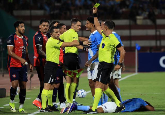 Argentine referee Dario Herrera shows a yellow card to Cerro Porteno's forward #10 Cecilio Dominguez (R) during the Copa Libertadores group stage football match between Peru's Sporting Cristal and Paraguay's Cerro Porteno at the Nacional stadium in Lima, on April 8, 2026. (Photo by Connie FRANCE / AFP)
