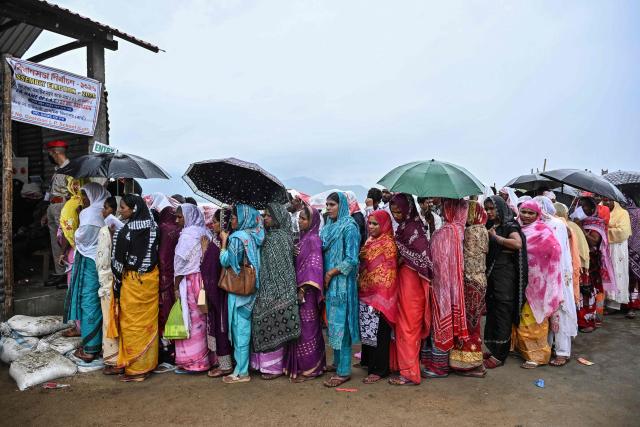 Voters stand in queues to cast their ballots to vote at a polling booth amid rainfall on an island in the middle of the river Brahmaputra during the Assam Legislative Assembly election in the Darrang district on April 9, 2026. (Photo by Biju BORO / AFP)
