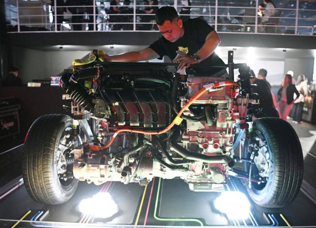 A worker cleans a skeletal model of an electric car engine made in China on display during the opening day of the International Auto Show in Manila on April 9, 2026. (Photo by Ted ALJIBE / AFP)