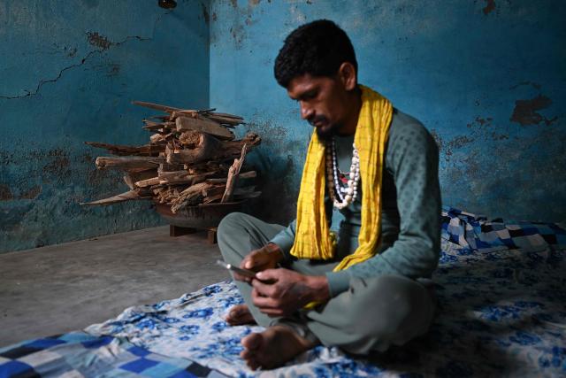 A migrant worker sits beside firewood kept inside his rented room in New Delhi on April 9, 2026. (Photo by Sajjad HUSSAIN / AFP)
