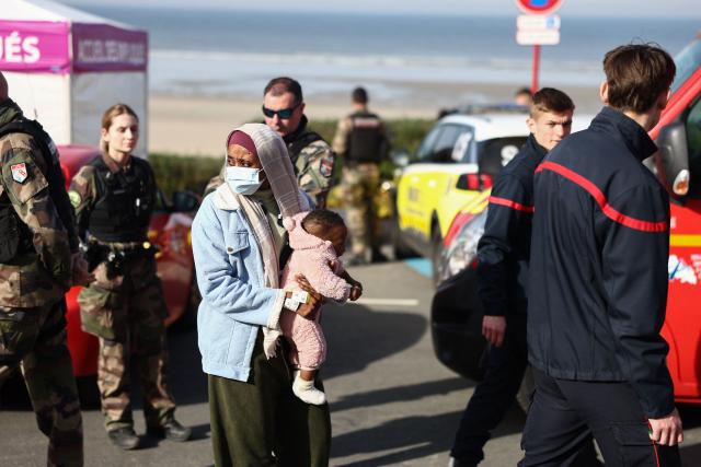 A woman with a baby stands next to rescue units after an attempt to cross the English Channel illegally turned tragic with several migrants found in cardiac arrest, in France's Pas-de-Calais northern coastal city of Equihen-Plage on April 9, 2026. Two men and two women died on April 9, 2026 morning whilst attempting to cross the English Channel illegally; they were ‘swept away’ by the currents off the coast of Equihen-Plage (Pas-de-Calais), announced Franзois-Xavier Lauch, the Prefect of Pas-de-Calais, at the scene. (Photo by Sameer AL-DOUMY / AFP)