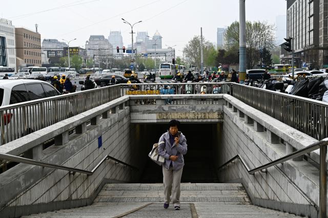 A woman exits an underground street crossing in Beijing on April 9, 2026. (Photo by Pedro PARDO / AFP)
