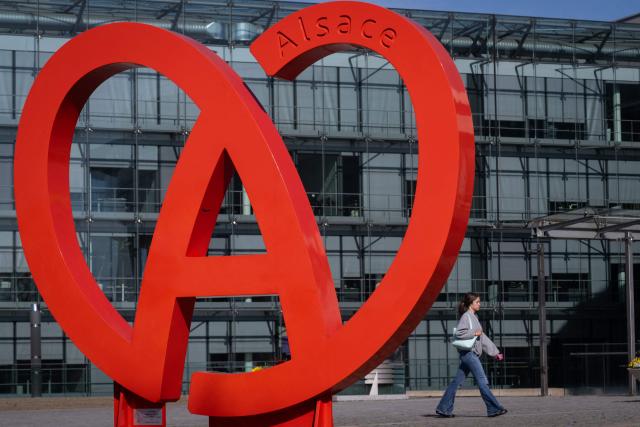 A woman passes by the logo of the Collectivite Europeene d'Alsace (CEA), on April 9, 2026, in Colmar, eastern France. France's parliament lower house, the National Assembly, passed on April 8, 2026 a revised version of the bill aimed at removing Alsace from the Grand Est region at its first reading, although the future of the bill remains uncertain at this stage. (Photo by SEBASTIEN BOZON / AFP)