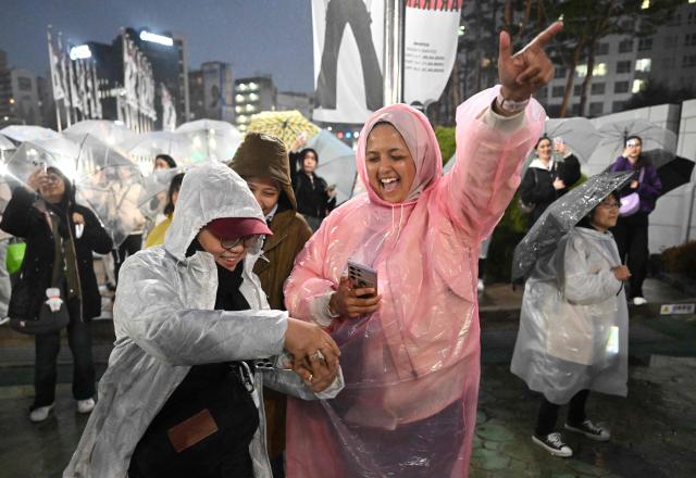 BTS fans react as they watch a live concert by K-pop boy band BTS on their mobile phones outside a stadium where the group is performing in Goyang on April 9, 2026. South Korean K-pop megastars BTS kicked off their world tour on April 9, riding the momentum of a chart-topping comeback album and a landmark performance in the heart of Seoul. (Photo by Jung Yeon-je / AFP)