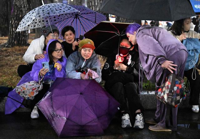 BTS fans react as they watch a live concert by K-pop boy band BTS on their mobile phones outside a stadium where the group is performing in Goyang on April 9, 2026. South Korean K-pop megastars BTS kicked off their world tour on April 9, riding the momentum of a chart-topping comeback album and a landmark performance in the heart of Seoul. (Photo by Jung Yeon-je / AFP)