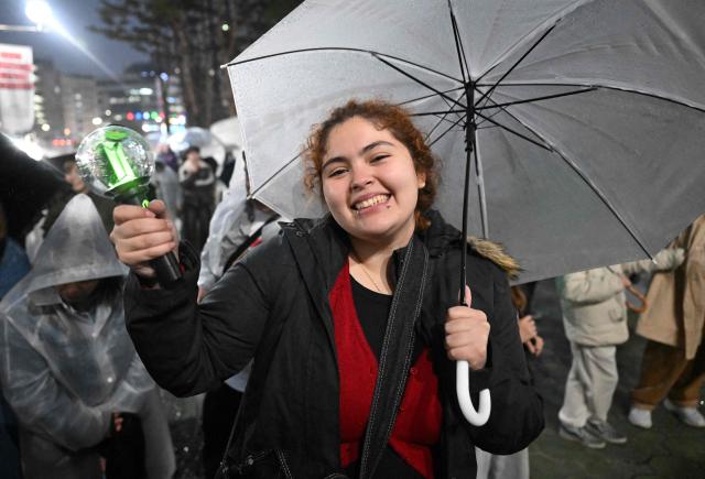 A BTS fan reacts as she listens to a concert by K-pop boy band BTS outside a stadium where the group is performing in Goyang on April 9, 2026. South Korean K-pop megastars BTS kicked off their world tour on April 9, riding the momentum of a chart-topping comeback album and a landmark performance in the heart of Seoul. (Photo by Jung Yeon-je / AFP)