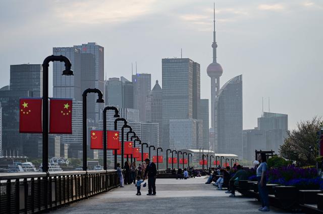 People walk along the Huangpu River as the city's skyline is seen in Shanghai on April 9, 2026. (Photo by Jade GAO / AFP)