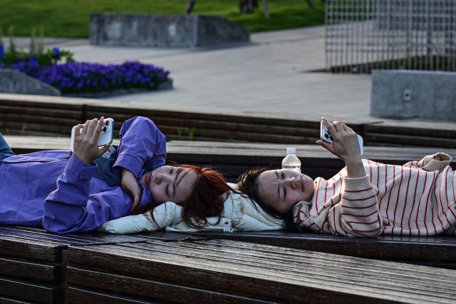 Two women lying on a bench look at their phones along the Huangpu River in Shanghai on April 9, 2026. (Photo by Jade GAO / AFP)