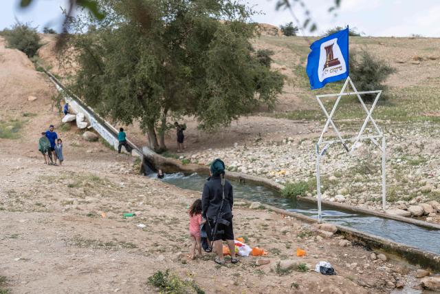 An armed Israeli settler gathers with others at a water slide in the Israeli-occupied West Bank village of Ras Ein al-Auja on April on April 9, 2026. Israel vowed more strikes against Hezbollah on April 9, dismissing mounting international demands that the fragile truce between the United States and Iran in the Gulf be expanded to cover the war in Lebanon. (Photo by Ilia YEFIMOVICH / AFP)
