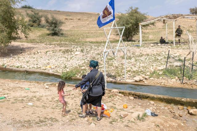 An armed Israeli settler stands with children near a water slide in the Israeli-occupied West Bank village of Ras Ein al-Auja on April on April 9, 2026. Israel vowed more strikes against Hezbollah on April 9, dismissing mounting international demands that the fragile truce between the United States and Iran in the Gulf be expanded to cover the war in Lebanon. (Photo by Ilia YEFIMOVICH / AFP)