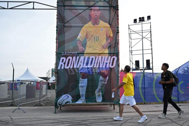 Men walk past a banner depicting Brazilian formar footballer Ronaldinho Gaucho during the Legends Football Tournament in Willemstad, Curacao, in the Dutch Caribbean, on April 8, 2026. (Photo by Raul ARBOLEDA / AFP)