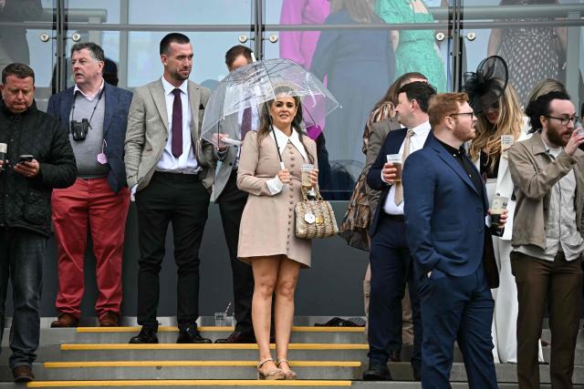 A woman (C) uses an umbrella in cool, wet weather on the opening day of the Grand National Festival horse race meeting at Aintree Racecourse in Liverpool, north-west England, on April 9, 2026. (Photo by Paul ELLIS / AFP)