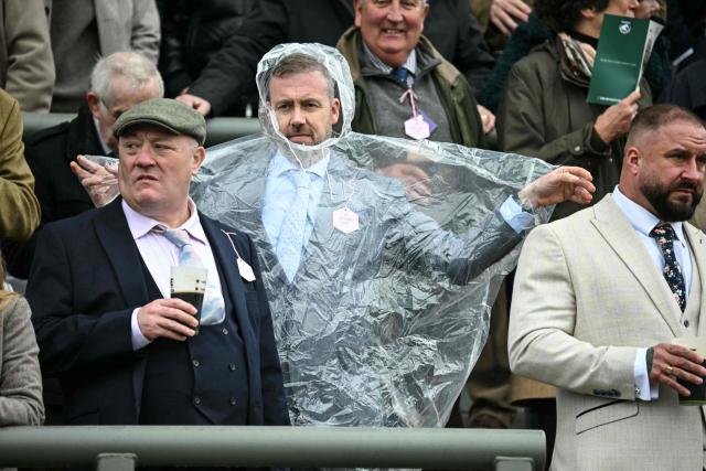 A man puts on a plastic poncho on the opening day of the Grand National Festival horse race meeting at Aintree Racecourse in Liverpool, north-west England, on April 9, 2026. (Photo by Paul ELLIS / AFP)